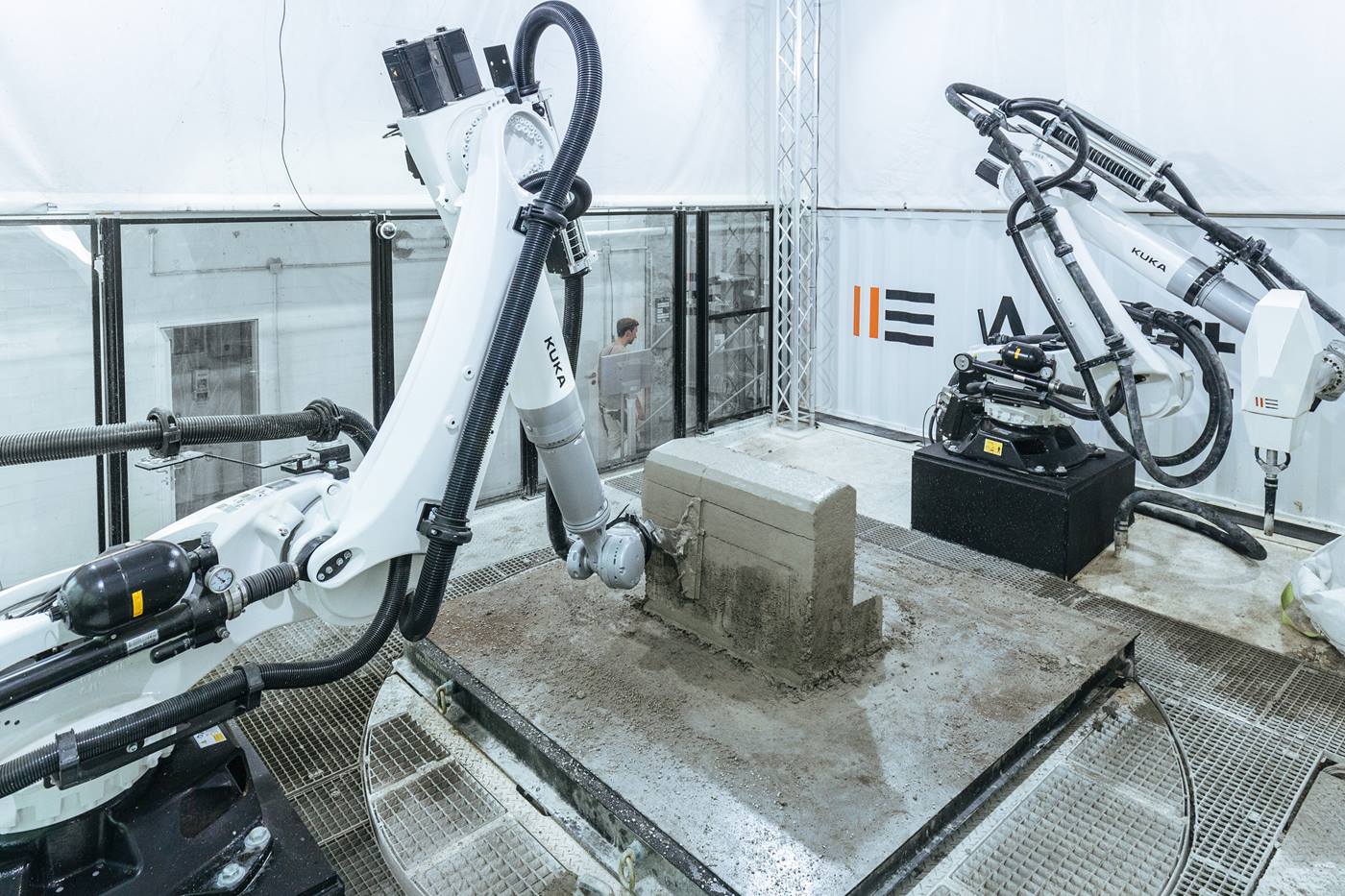 De eerste robot brengt bij het 3D-printen in de bouw het spuitbeton aan, daarna strijkt de tweede robot het oppervlak glad.