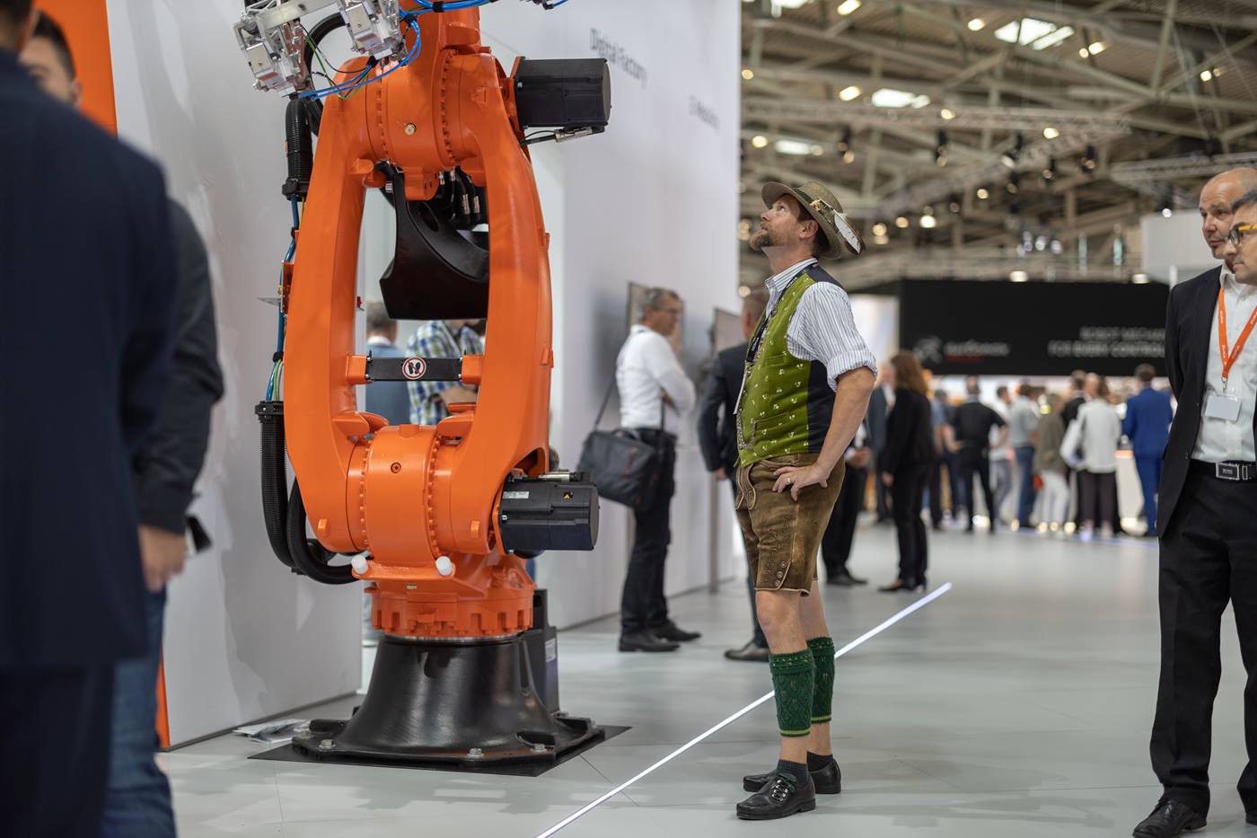 Man in lederhosen looks at a KUKA robot at the automatica trade fair in Munich.