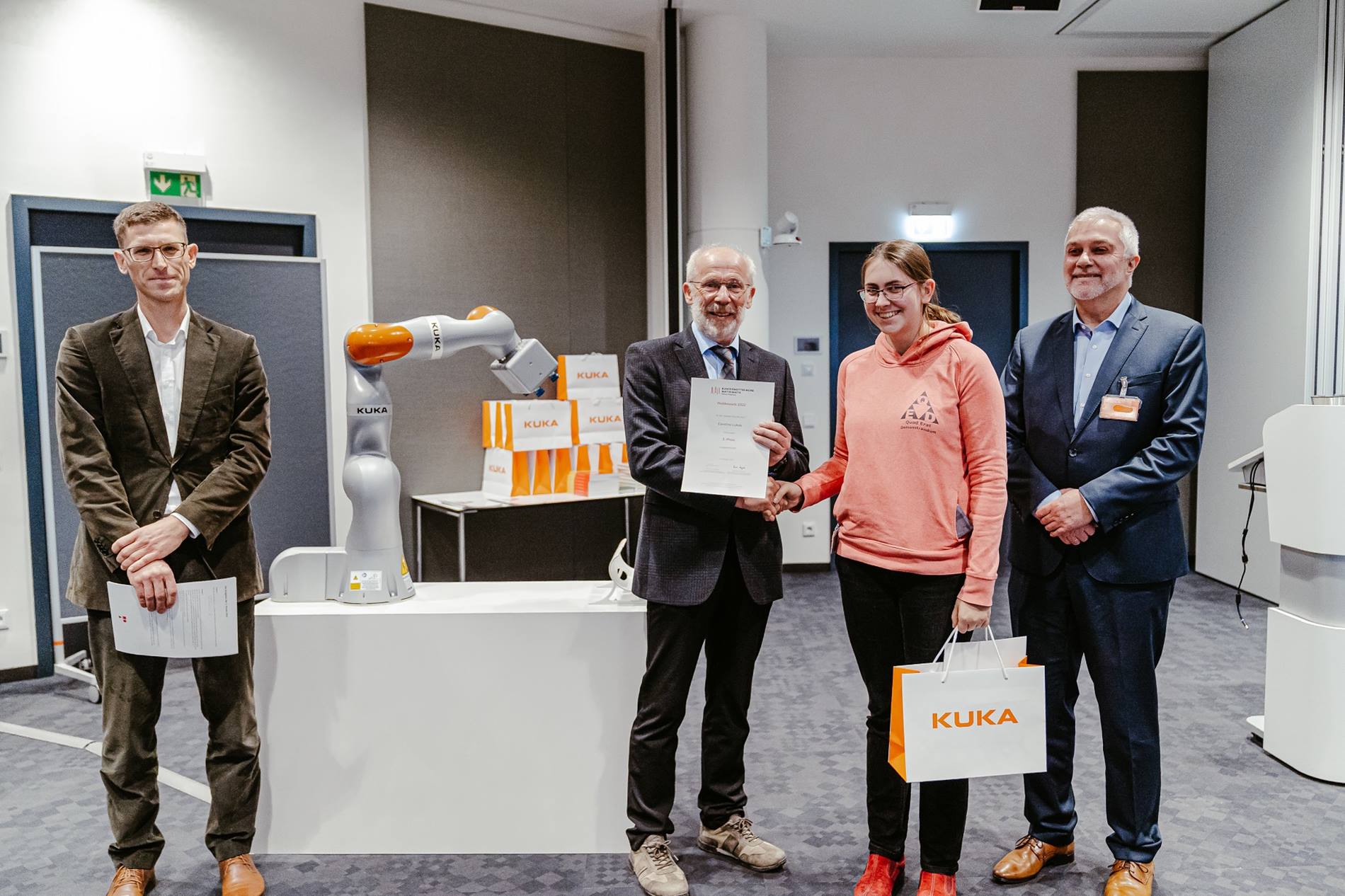 Bei der Preisverleihung des Bundeswettbewerbs für Mathematik wird einer Gewinnerin ihre Auszeichnung verliehen, mit im Bild ein KUKA Roboter LBRiisy