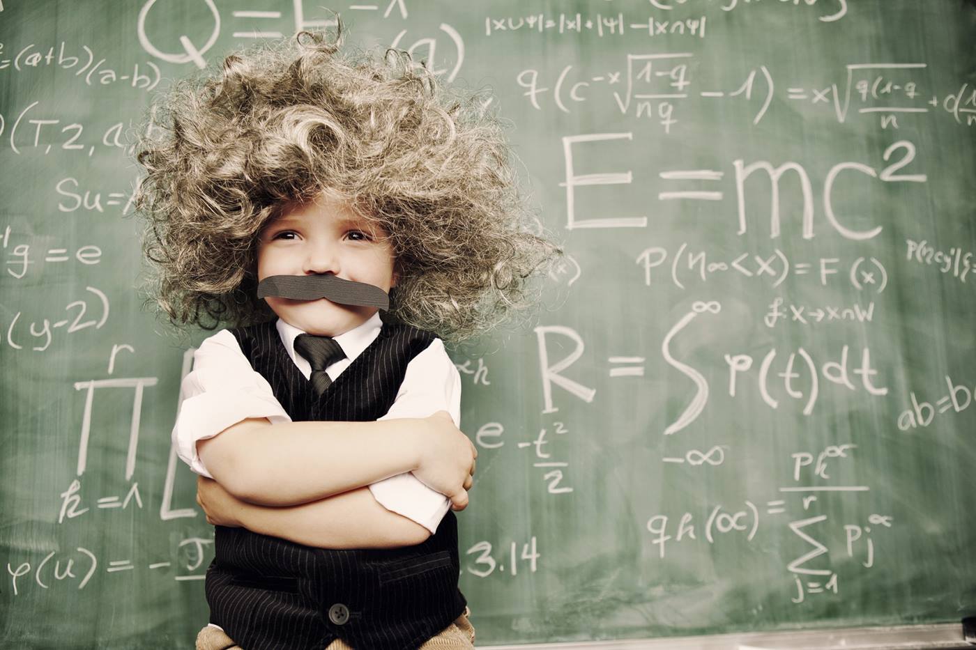 Kind mit verschränkten Armen und Schnurrbart, das an Albert Einstein erinnert, steht vor einer Tafel mit mathematischen Gleichungen. 