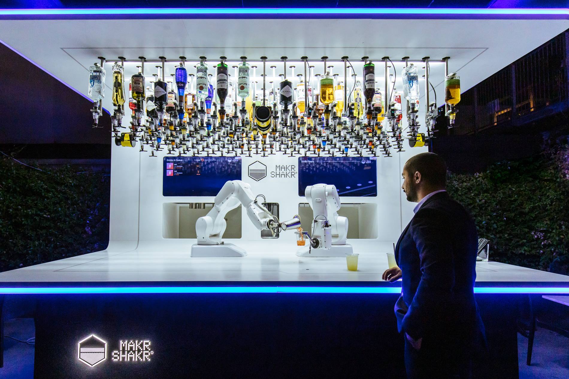 Two KUKA robots mix a cocktail together at a bar counter.