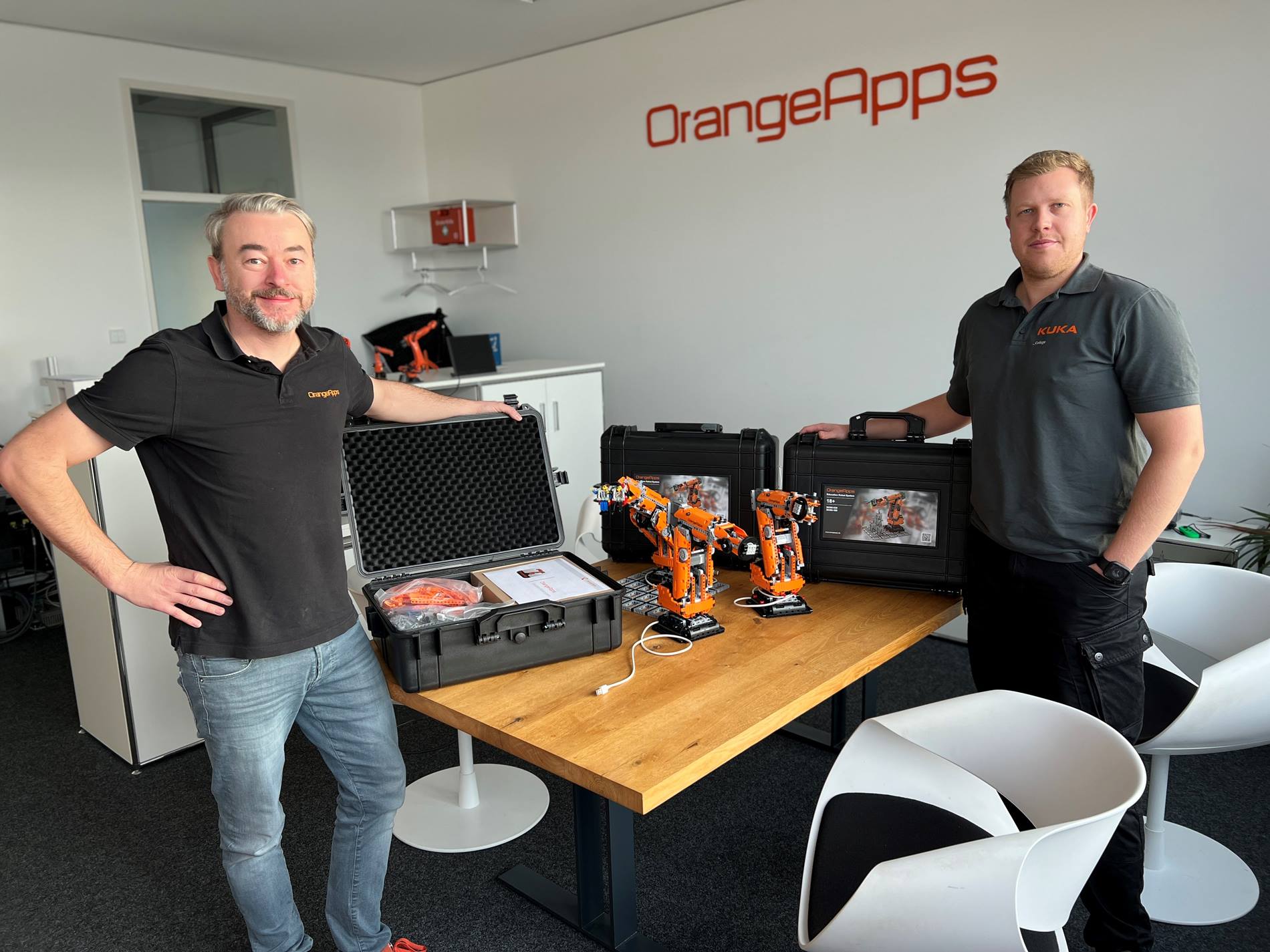 Daniel Schmidt, Geschäftsführer von OrangeApps überreicht Maximilian Kruse, Roboter-Trainer am KUKA College Augsburg, einen Baustein-Roboter.