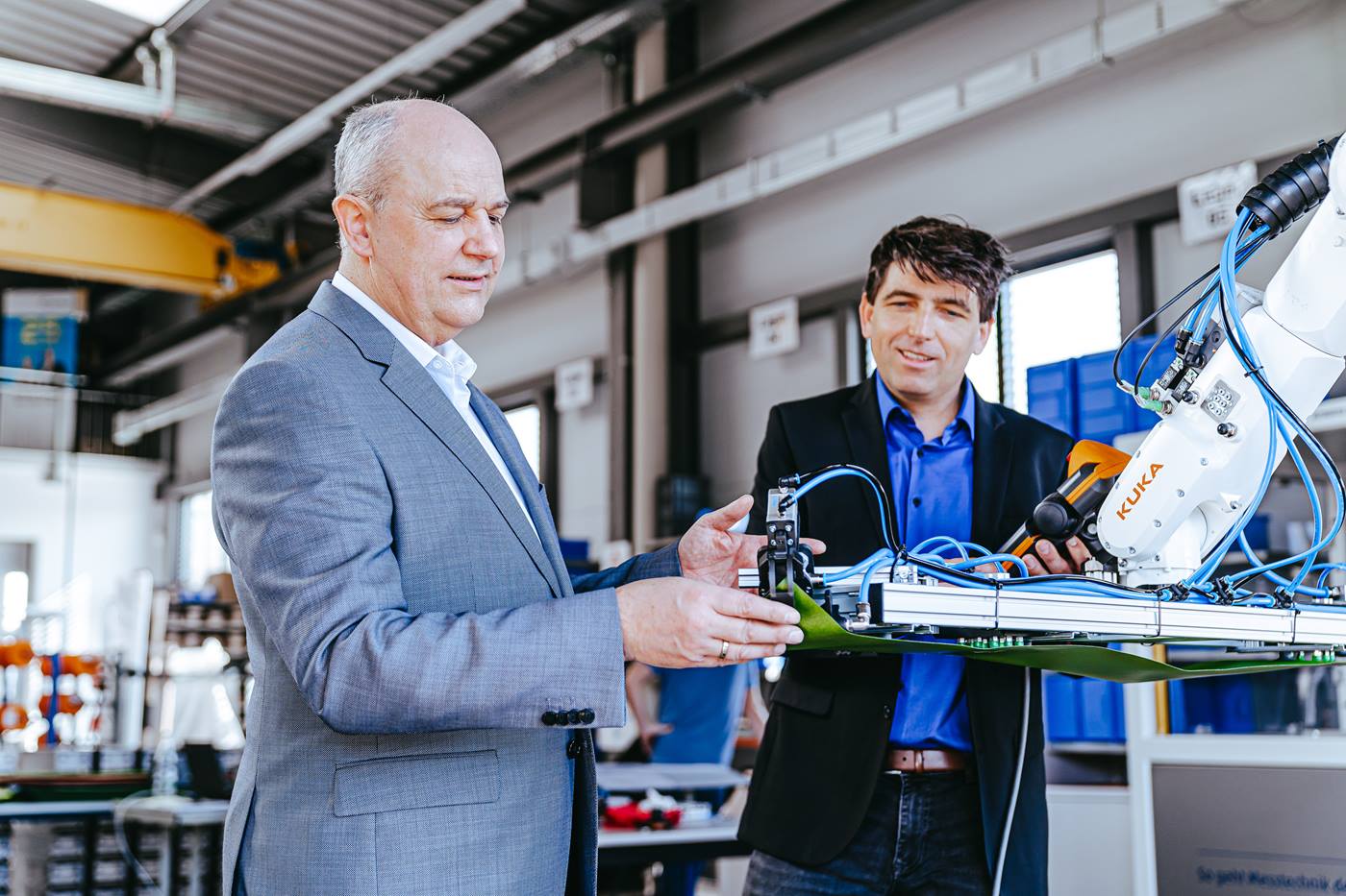 Michael Fraede und Michael Müller, die Gründer von robotextile, begutachten einen KUKA Roboter der in einer Textilproduktion arbeitet.  