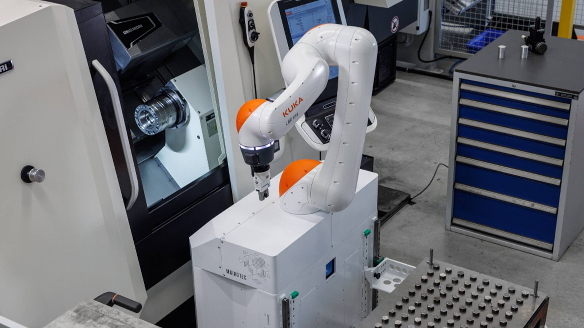 CNC-Fräse wird von Cobot mit Metallblöcken beladen.